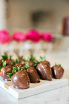 Chocolate covered strawberries on a marble tray with pink flowers blurred in the background