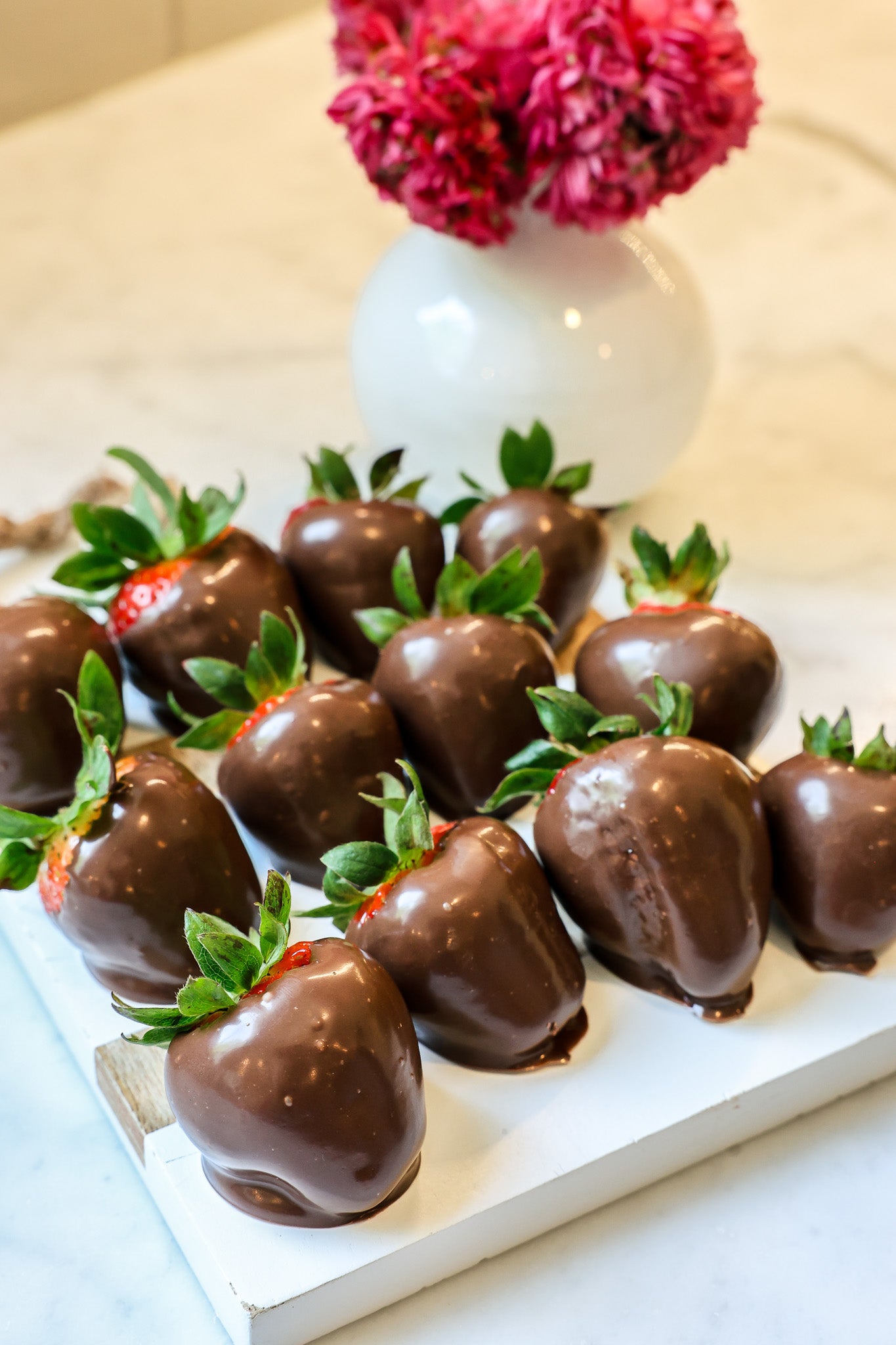 Chocolate dipped strawberries on a white tray with pink flowers in the background