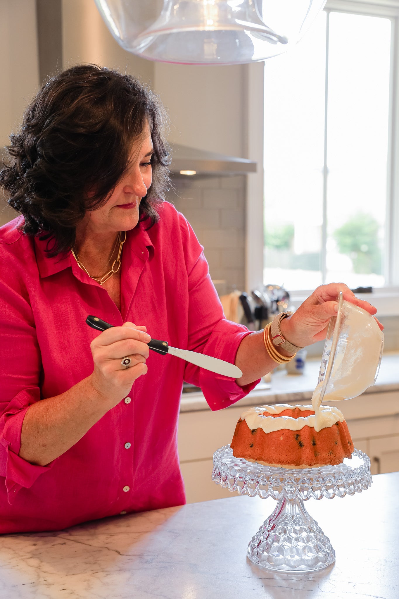 Charlee Rodgers pouring icing over a pound cake on a pedestal in her kitchen