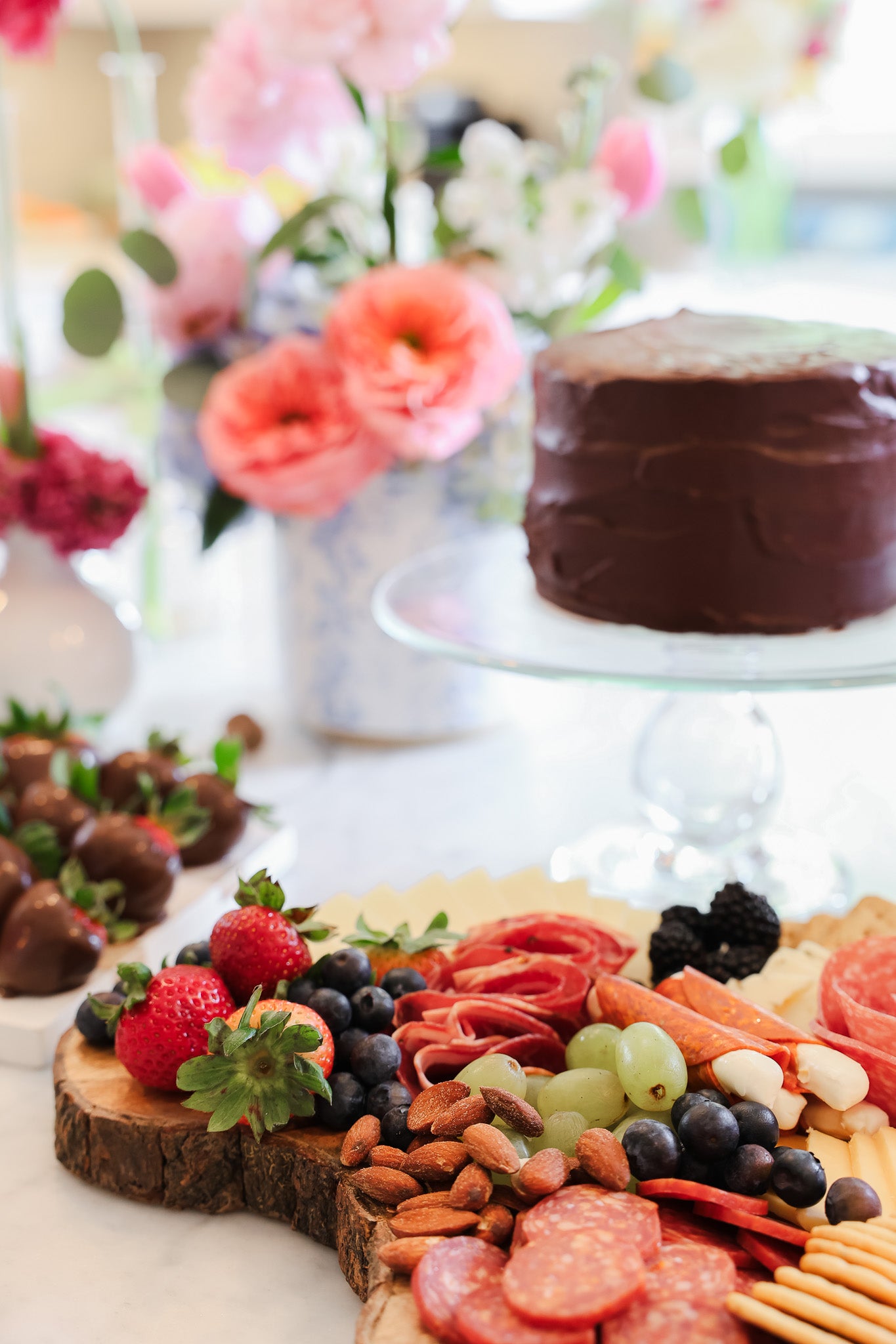 A charcuterie board, chocolate covered strawberries, chocolate cake and flowers