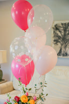 Various shades of pink and white balloons with flowers at the bottom of the photo