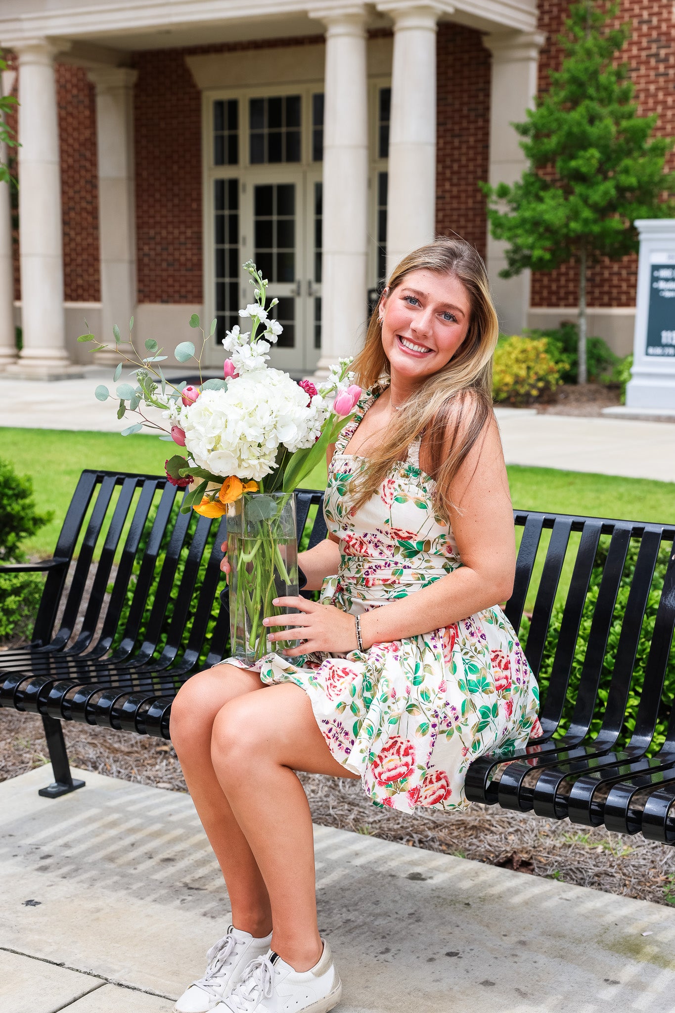 Camryn holding flowers and sitting on a bench outside of Tutwiler Hall on University of Alabama's campus