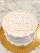 Strawberry cake with white icing that says "Happy birthday Reese!" on a gold platter