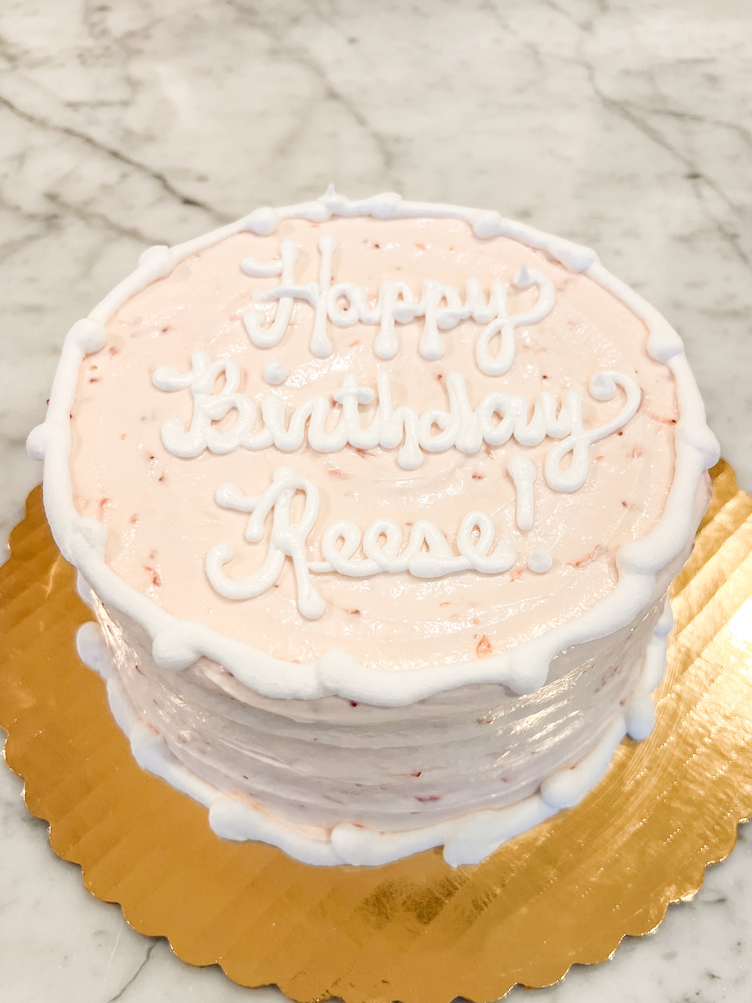 Strawberry cake with white icing that says "Happy birthday Reese!" on a gold platter