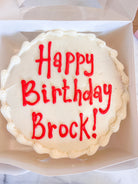 Cake with white icing that says "Happy Birthday Brock!" in red icing