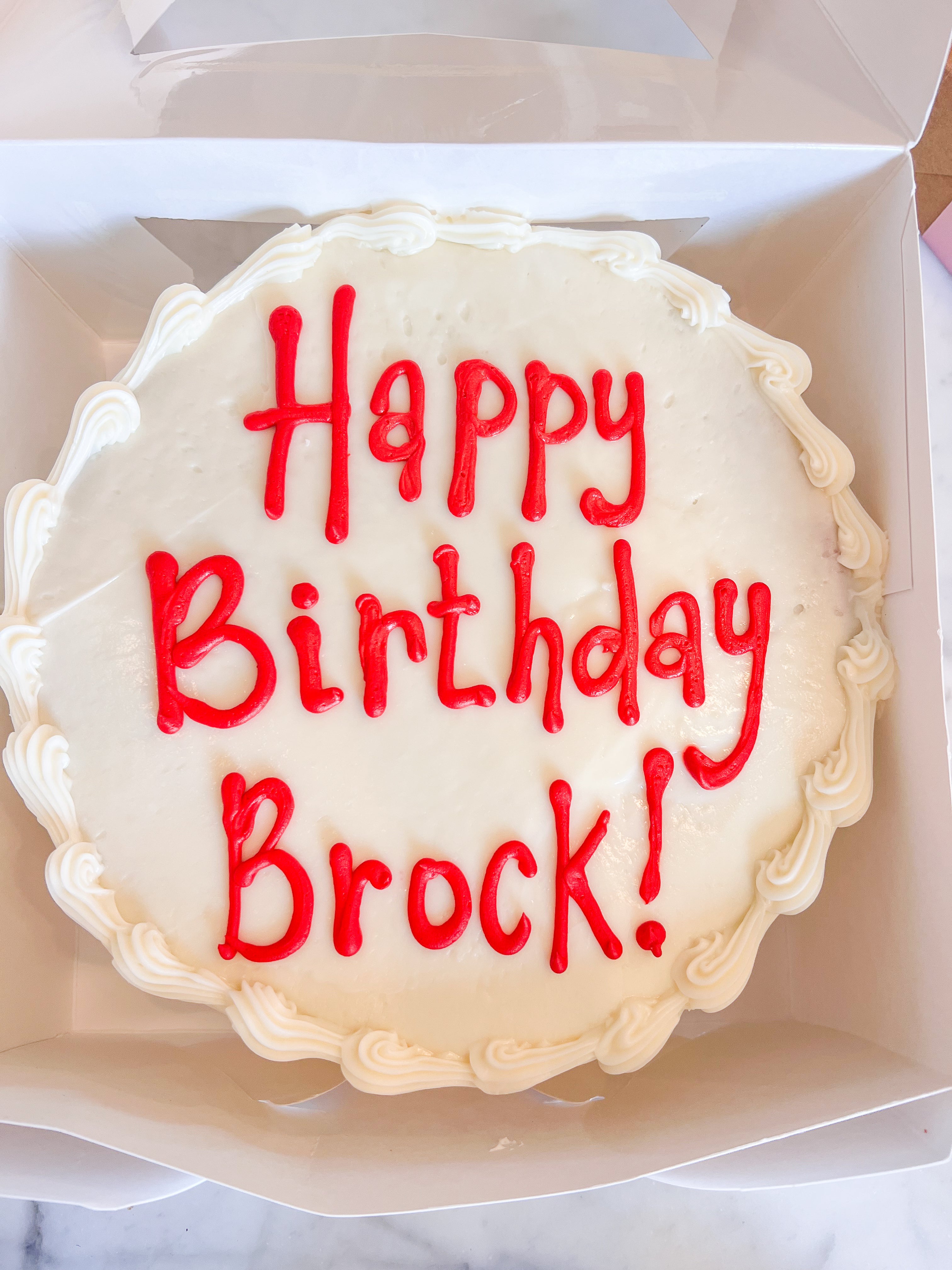 Cake with white icing that says "Happy Birthday Brock!" in red icing